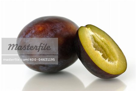 A whole and a bisected blue plum before white background.