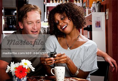 Caucasian man and African American woman in coffee house with cell phone