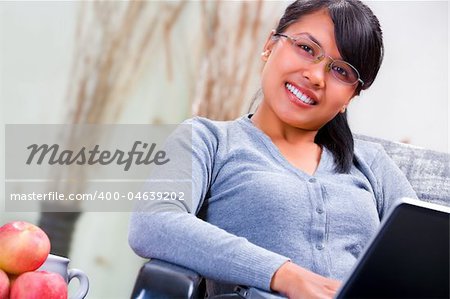 Portrait of a young Asian woman with her laptop sitting on sofa at home.