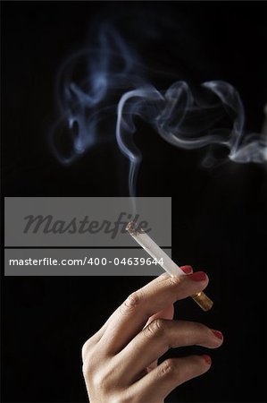 finger holding burning cigarette against dark