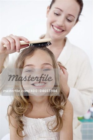 Portrait of mother doing her little daughter's hair in bathroom