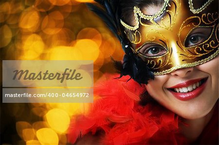Beautiful young woman in carnival mask over gold background
