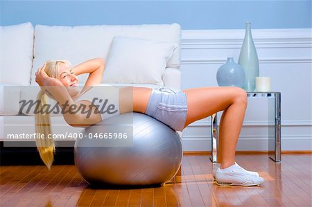 Side view of young woman wearing sportswear and doing crunches on a balance ball in living room.  Horizontal shot.