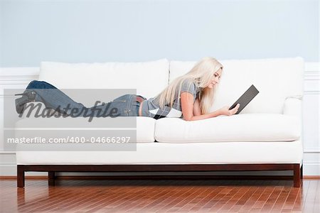 Full length view of woman lying on white couch and reading a book. Horizontal format.