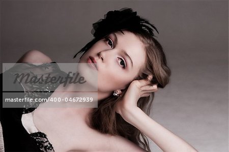 Attractive young woman lying down and resting her head on her hand. She is wearing a black lace top and a black feather hairdressing. Horizontal shot.