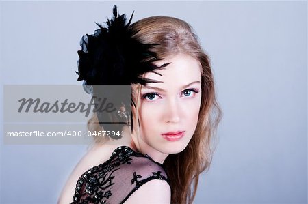 Attractive young woman wearing a black lace top and a black feather hairdressing. She is looking over her shoulder. Horizontal shot.