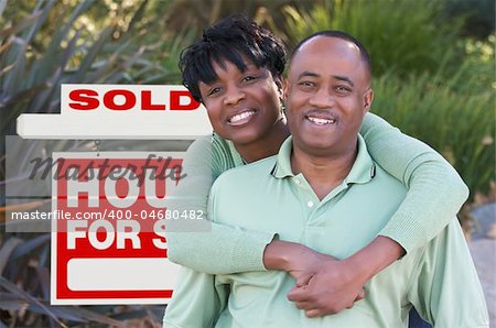 Happy African American Couple in Front of Sold Home For Sale Real Estate Sign.