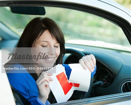 Brunette teen girl sitting in her car tearing a L-sign after having her driver's licence