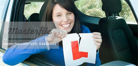 Smiling teen girl sitting in her car tearing a L-sign after having her driver's licence