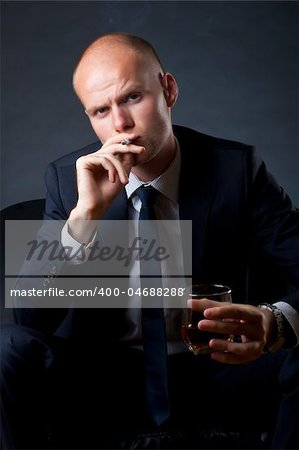 blue eyed businessman siting on a sofa and smoking a cigarette and drinking whiskey