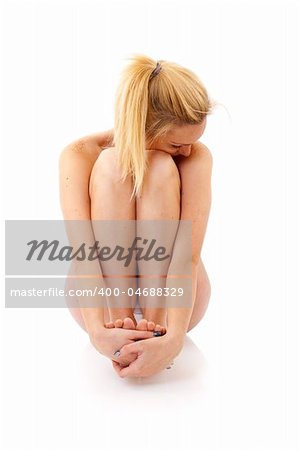 Young woman sitting and embracing her legs,  isolated on white background