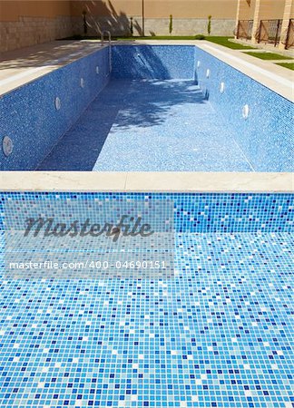 Blue tiled empty swimming pool on a sunny day without water