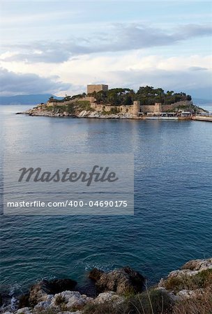 Pigeon Island Fortress, also known as the Pirates castle, in the Kusadasi harbor, on the Aegean coast of Turkey. Shallow DOF, focus on foreground rocks and water