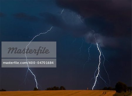 forks of bluish-white lightning strike on side of a dark highway at night