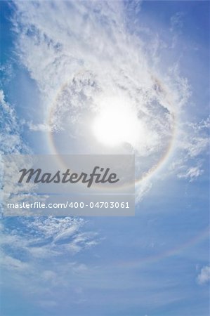 Sun with circular rainbow, clouds and blue sky