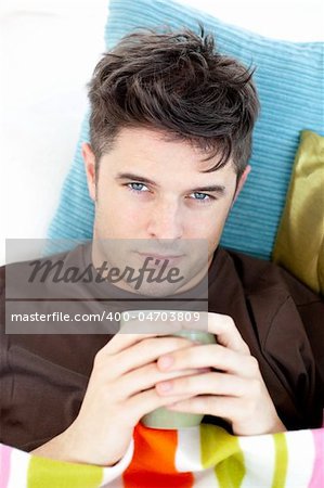 Sick man lying on a sofa holding a cup looking at the camera