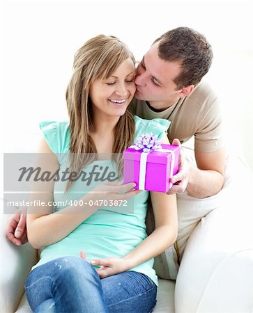 Attractive boyfriend giving a present and a kiss to his glowing girlfriend against white background