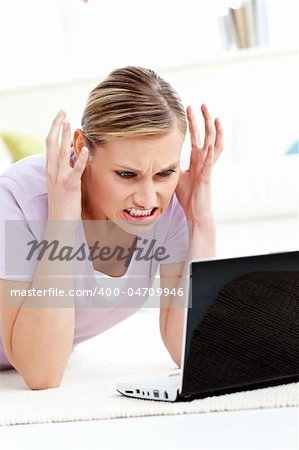 Angry young woman lying on the floor using her laptop in the living room