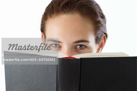 Teen girl, doing homework, looking at the camera over the book. Studio shot.