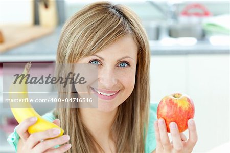 Positive caucasian woman holing a banana and an apple in the kitchen at home