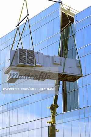crane lifting cooling unit air conditioning system up the side of glass  building