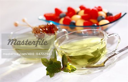 Two cups of green herbal tea with sugar stick and fresh fruits