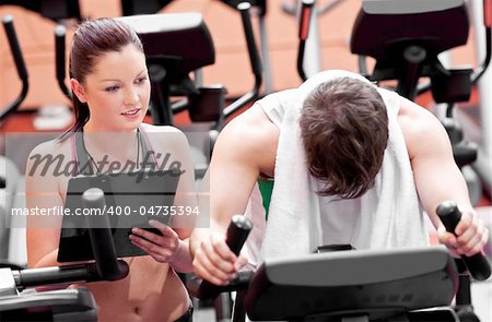 Exhausted man doing exercises while his coach is looking at his results in a sport centre