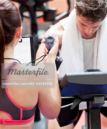 Close-up of a coach using a chronometer while man is doing physical exercises in a fitness centre