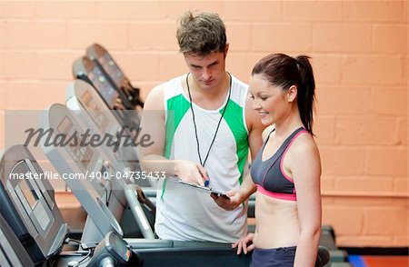 Serious coach giving instruction to a female athlete standing on a treadmill in a fitness centre