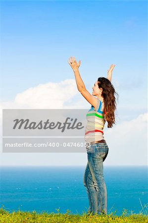 A young attractive woman with her hans in the air and smiling in front of a beautiful ocean