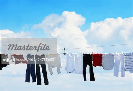 Pants and shirts on clothesline against beautiful white puffy cloud on a sunny day.