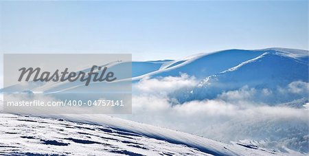 Panoramic view of snowy mountain ridges emerging from clouds