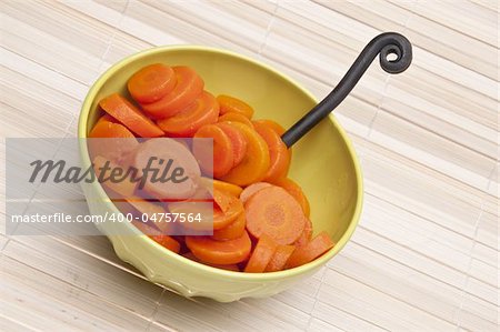 Bowl of canned carrots with fork on a bamboo mat background.