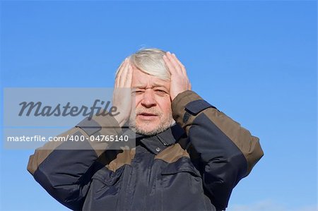 Portrait of mature desperate man with grey hair on blue sky of the background.