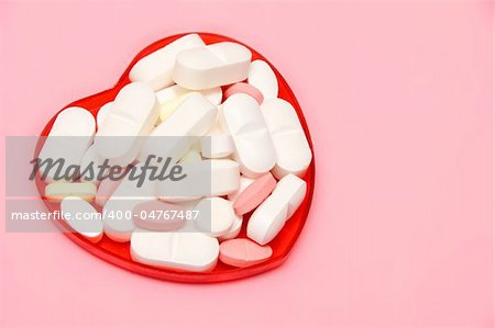 plastic heart holding some pills over pink