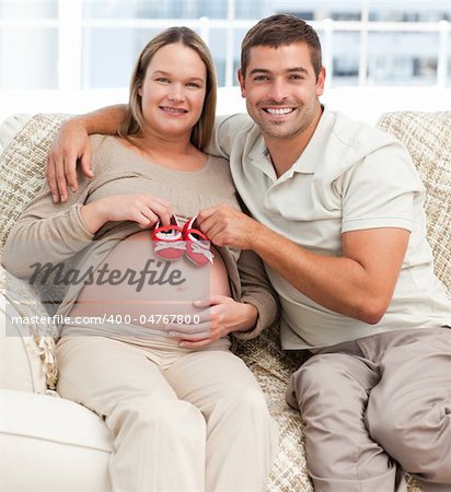 Lovely couple putting baby shoes on the woman's belly sitting in the living room