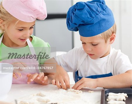 Young brother and sister kneading a dough to make cakes in the kitchen