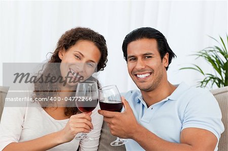 Happy couple drinking red wine sitting on the sofa at home