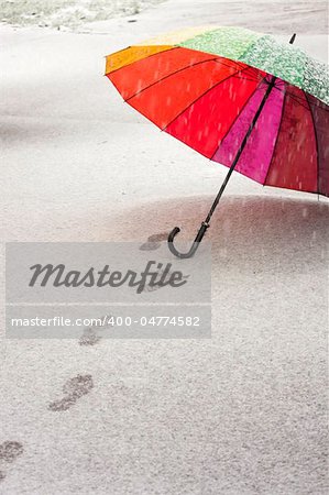 Colorful umbrella in the fresh fallen snow with some footprints around it.