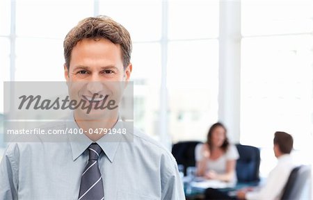 Happy businessman in the foreground while his team is working at a table