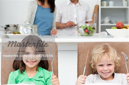 Impatient little brother and sister waiting for their lunch by playing with forks