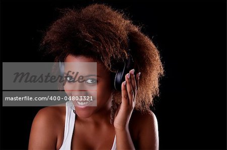 Beautiful black woman happy listening music in headphones, isolated on black background. Studio shot.