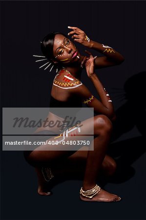 Beautiful exotic African female fashion with tribal yellow red and white makeup cosmetics and sticks in hair, in cultural dance position.