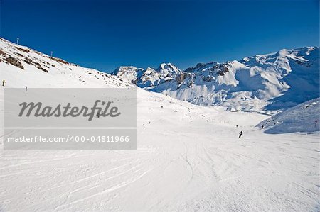 View down a piste with skiers and mountains