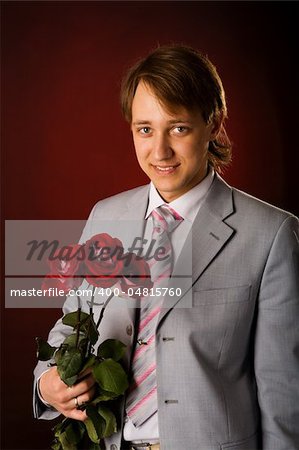 Young man wearing suit holding roses over red background