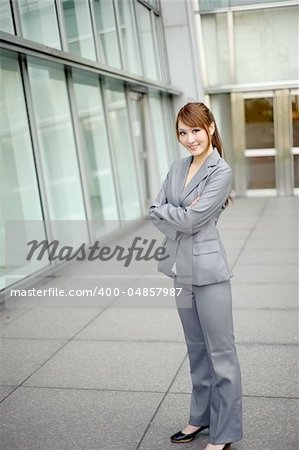 Young business manager with friendly expression on face, full length portrait outside of modern buildings.