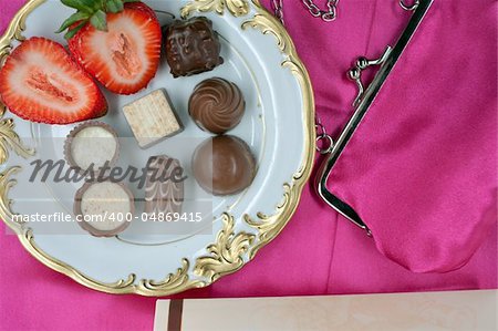 pralines decorated with a strawberry on a plate on table with purse