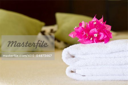 White towels with flowers on a bed in a hotel room. Selective focus on flowers.