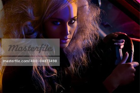 Beautiful blond high fashion model in car at night shot with colored lights.