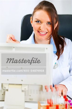 Smiling medical doctor woman sitting at office table and working on computer